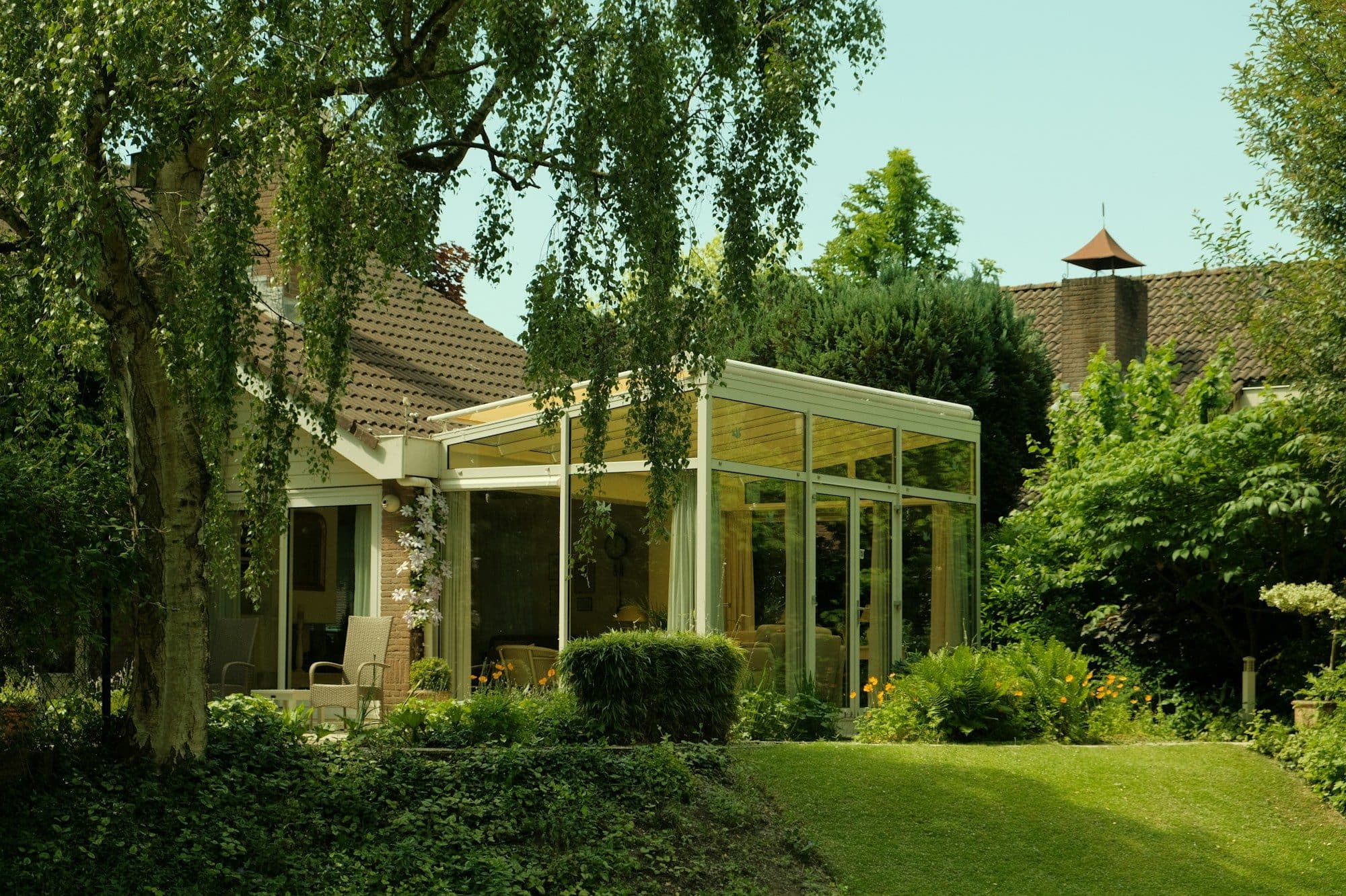 Verglaster Anbau an einem Wohnhaus, umgeben von Garten und Bäumen